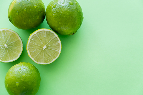 Top view of organic limes with water drops on green background with copy space