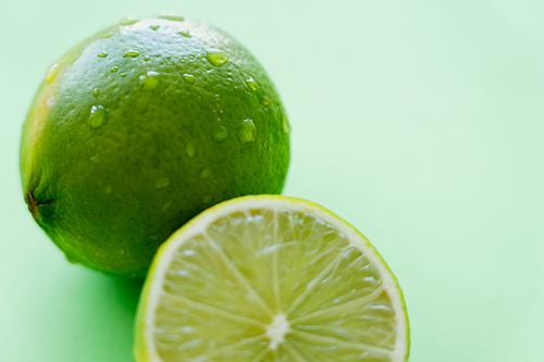Close up view of fresh lime with water drops on peel on green background