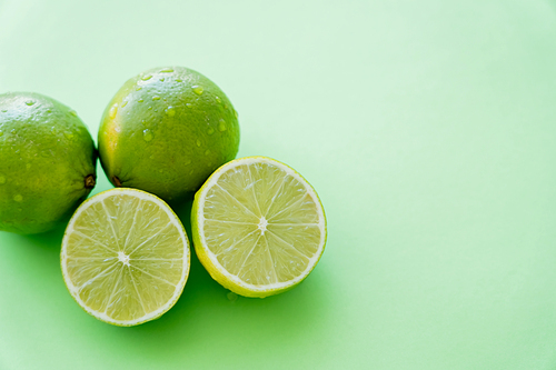 Top view of organic limes with droplets on peel on green background