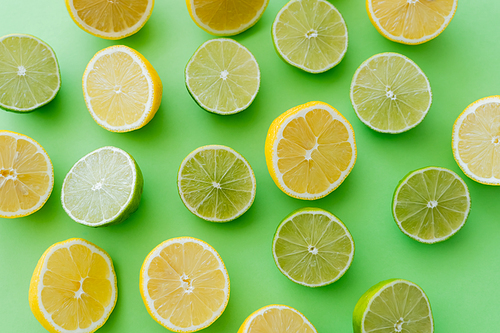 Top view of cut limes and lemons on green background