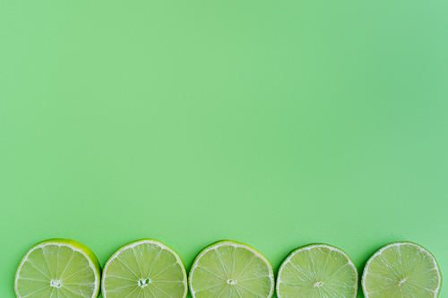 Top view of slices of limes on green background with copy space