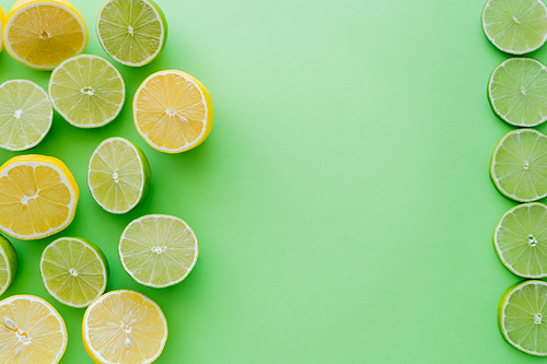 Top view of cut and slices of lemons and limes on green background