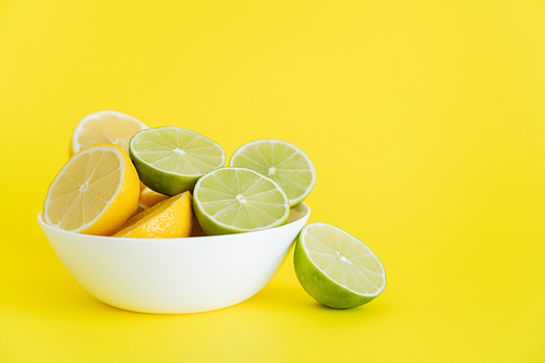 Fresh halves of limes and lemons in bowl on yellow background