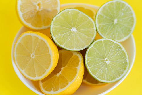 Top view of fresh lemons and limes in bowl on yellow background