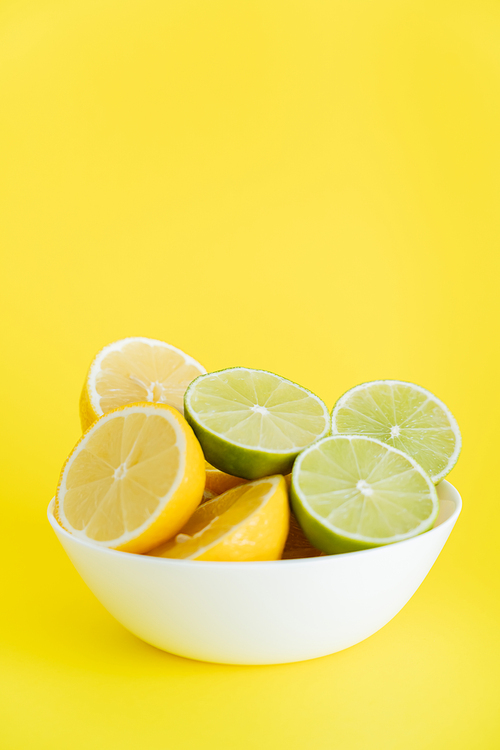 Bowl with cut lemons and limes on yellow background with copy space
