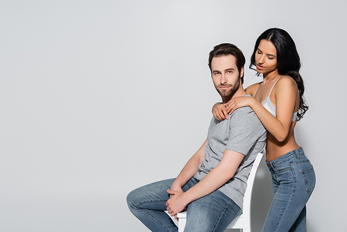 hot woman in bra and jeans embracing young man sitting on chair and  on grey