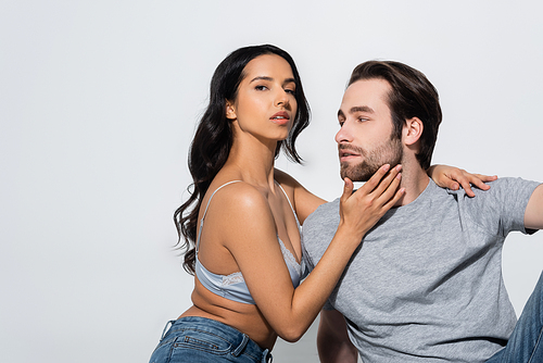 passionate brunette woman in jeans and bra touching face of young man while  isolated on grey