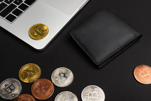 KYIV, UKRAINE - APRIL 26, 2022: High angle view of bitcoins near wallet and laptop on black background