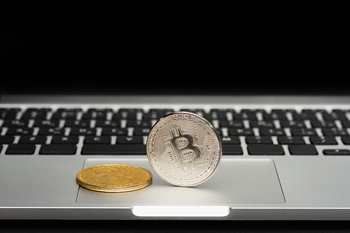KYIV, UKRAINE - APRIL 26, 2022: Close up view of bitcoins on blurred laptop isolated on black