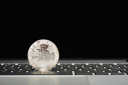 KYIV, UKRAINE - APRIL 26, 2022: Close up view of silver bitcoin on laptop keyboard on black background