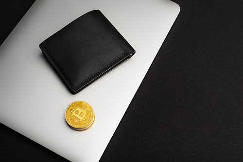 KYIV, UKRAINE - APRIL 26, 2022: Top view of wallet and bitcoins on laptop isolated on black