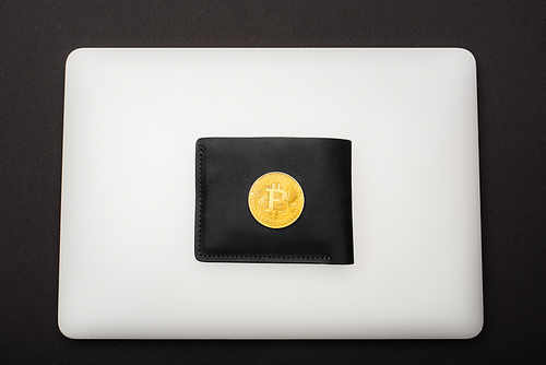 KYIV, UKRAINE - APRIL 26, 2022: Top view of golden bitcoin on wallet and laptop isolated on black