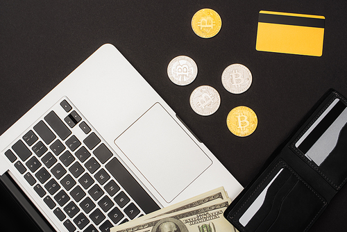 KYIV, UKRAINE - APRIL 26, 2022: Top view of dollars near credit card with laptop and bitcoins on black background