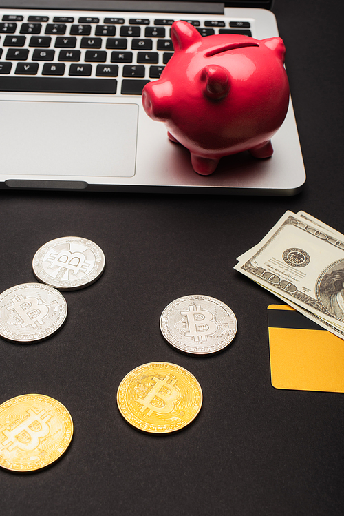 KYIV, UKRAINE - APRIL 26, 2022: High angle view of bitcoins near dollars and blurred laptop on black background