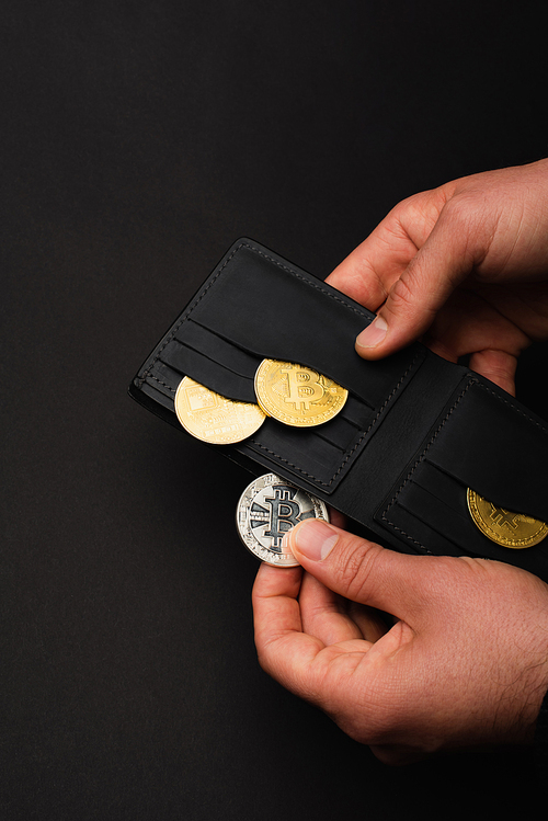 KYIV, UKRAINE - APRIL 26, 2022: Cropped view of man holding silver bitcoin and wallet isolated on black