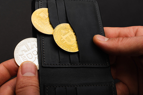 KYIV, UKRAINE - APRIL 26, 2022: Cropped view of man holding crypto coins and wallet isolated on black