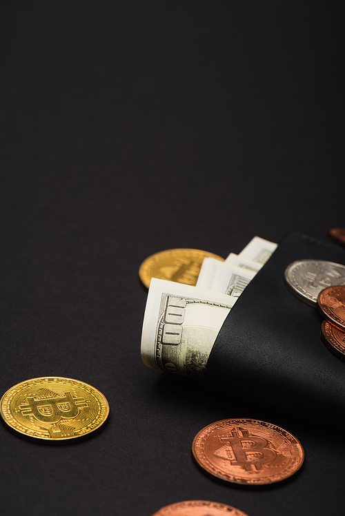 KYIV, UKRAINE - APRIL 26, 2022: Close up view of different bitcoins and dollars in wallet on black background