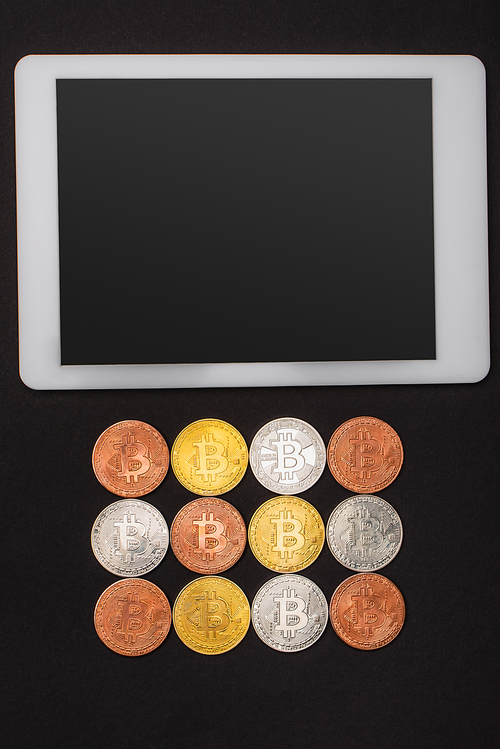KYIV, UKRAINE - APRIL 26, 2022: Top view of digital tablet with blank screen near bitcoins isolated on black