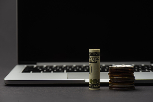 KYIV, UKRAINE - APRIL 26, 2022: Close up view of dollar near bitcoins and blurred laptop on black background