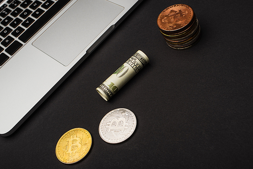 KYIV, UKRAINE - APRIL 26, 2022: Top view of dollar near bitcoins and laptop on black background