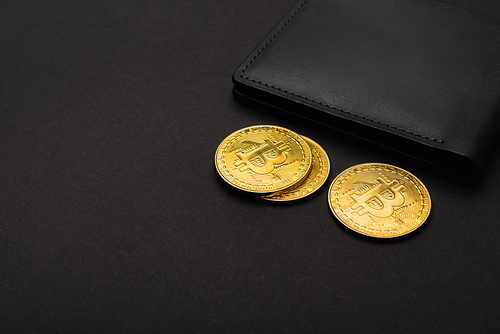 KYIV, UKRAINE - APRIL 26, 2022: Close up view of golden bitcoins near wallet on black background