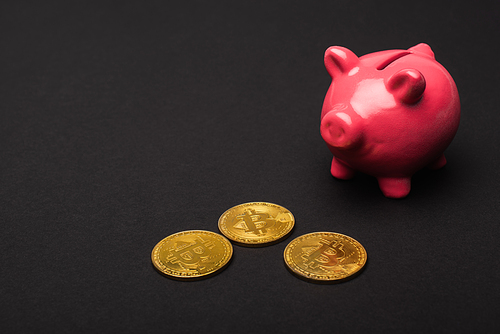 KYIV, UKRAINE - APRIL 26, 2022: Close up view of golden bitcoins and piggy bank on black background