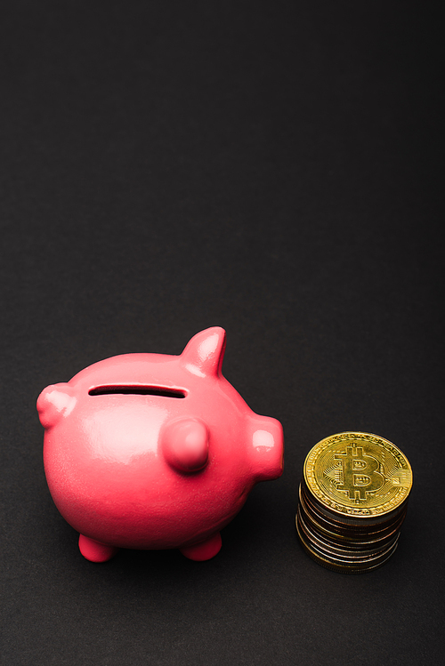 KYIV, UKRAINE - APRIL 26, 2022: Close up view of pink piggy bank near bitcoins on black background