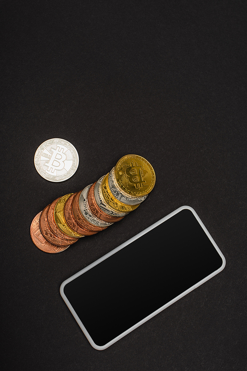 KYIV, UKRAINE - APRIL 26, 2022: Top view of crypto coins near smartphone with blank screen on black background