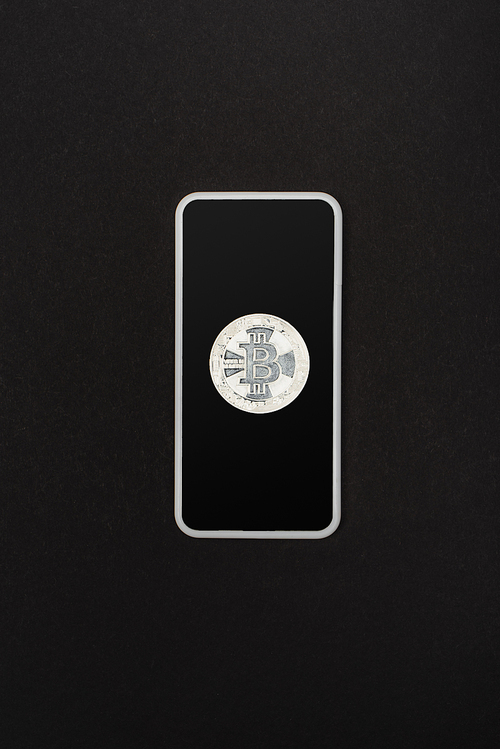KYIV, UKRAINE - APRIL 26, 2022: Top view of silver bitcoin on smartphone isolated on black