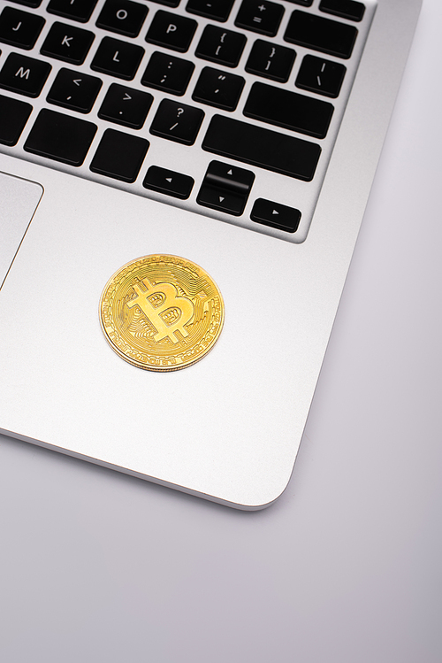 KYIV, UKRAINE - APRIL 26, 2022: Top view of golden bitcoin on laptop on grey background