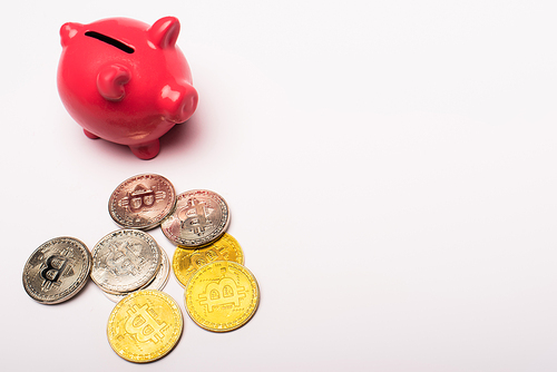 KYIV, UKRAINE - APRIL 26, 2022: High angle view of cryptocurrency and pink piggy bank on white background