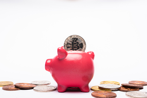 KYIV, UKRAINE - APRIL 26, 2022: Close up view of bitcoin in piggy bank near cryptocurrency on white background