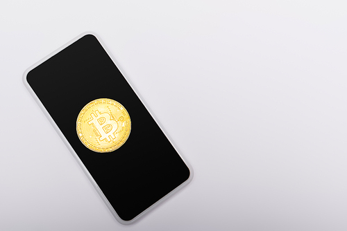 KYIV, UKRAINE - APRIL 26, 2022: Top view of golden bitcoin on smartphone on grey background