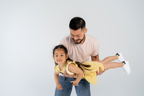 happy asian man holding in arms cheerful daughter in yellow dress isolated on grey