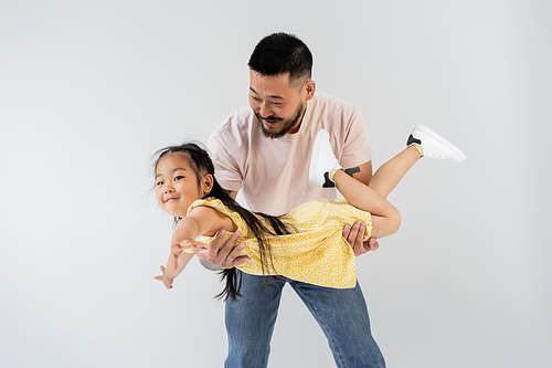 cheerful asian man holding in arms smiling daughter in yellow dress isolated on grey