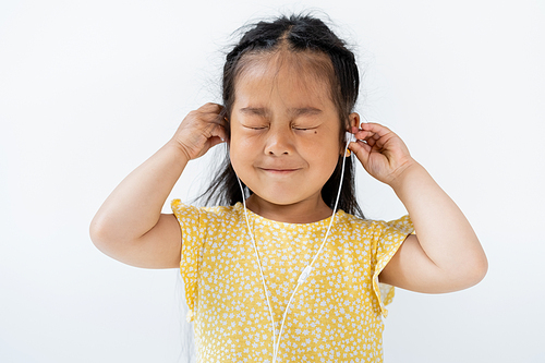 pleased asian girl with closed eyes wearing wired earphones isolated on grey