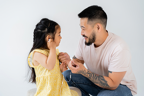 tattooed asian man holding wired earphones near daughter isolated on grey