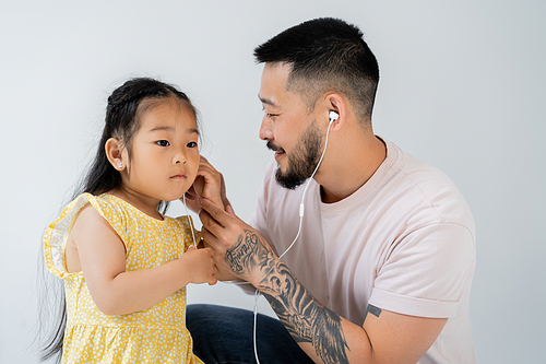 tattooed asian man wearing wired earphones near daughter isolated on grey