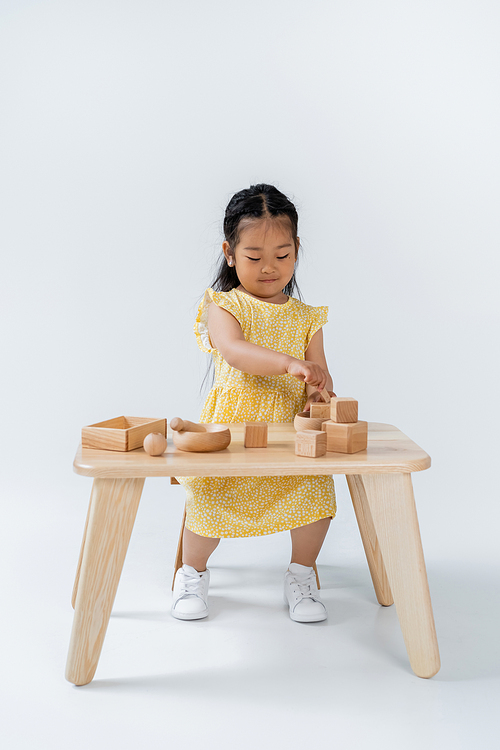 full length of asian child playing with wooden toys on table on grey