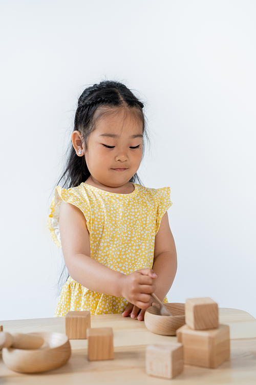 brunette asian girl holding wooden spoon near bowl while playing isolated on grey