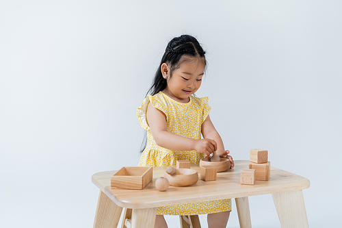 happy asian girl holding wooden spoon near bowl while playing isolated on grey