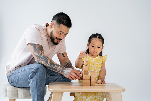 smiling asian father playing wooden cubes with preschooler daughter isolated on grey