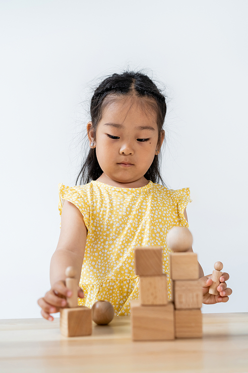 asian preschooler kid in yellow dress playing with blurred wooden shapes isolated on grey