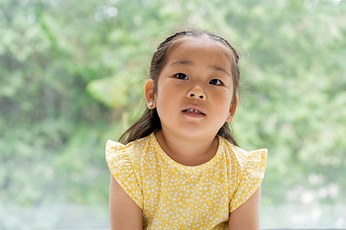 portrait of brunette and preschooler asian girl in yellow dress near window at home
