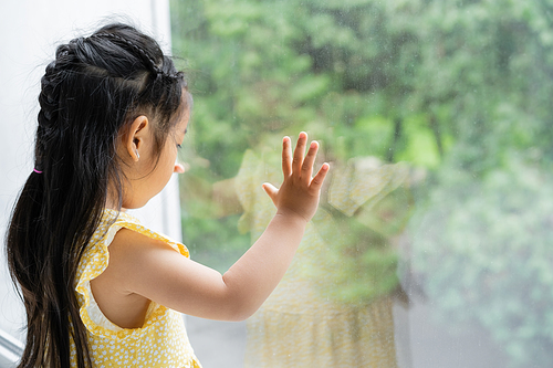 brunette and preschooler asian girl in yellow dress looking through window at home