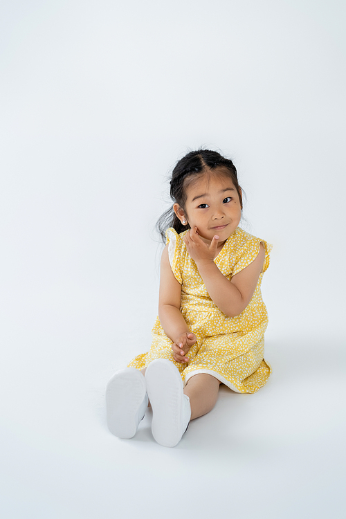 full length of cute asian child in yellow dress sitting on grey