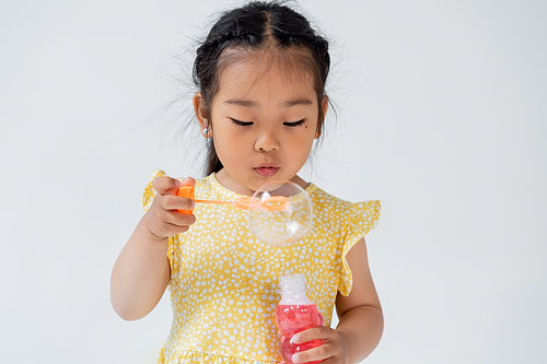 preschooler asian girl in dress holding bottle with soap bubbles isolated on grey