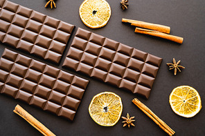 Top view of chocolate bars, spices and dry orange slices on black background