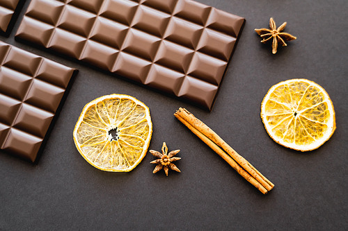 Top view of dry orange slices, spices and chocolate bars on black background
