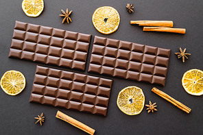Top view of chocolate bars, dry orange and spices on black background
